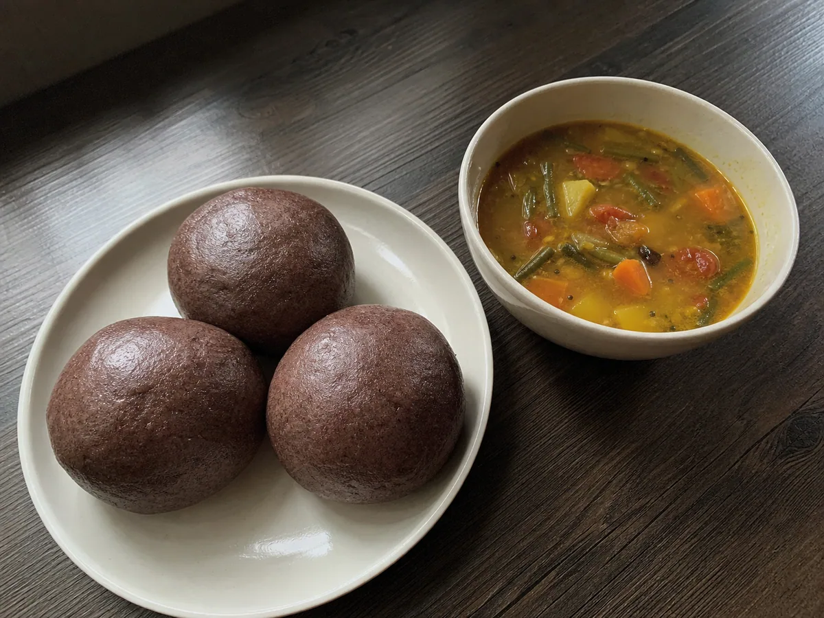 Portioned ragi dough with one smooth mudde ball shaped on a lightly damp plate