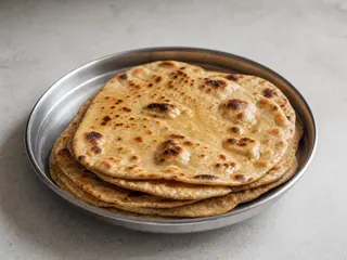 Pila de naan de trigo integral con ampollas doradas y un ligero brillo de mantequilla