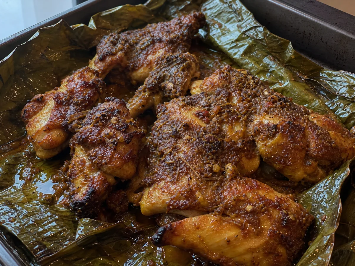 Pollo ayam betutu completamente cocido y dorado en una fuente abierta forrada con hoja de plátano