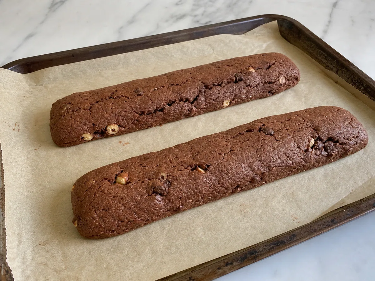 Fully baked cocoa biscotti logs with matte tops, firm edges, and fine surface cracks