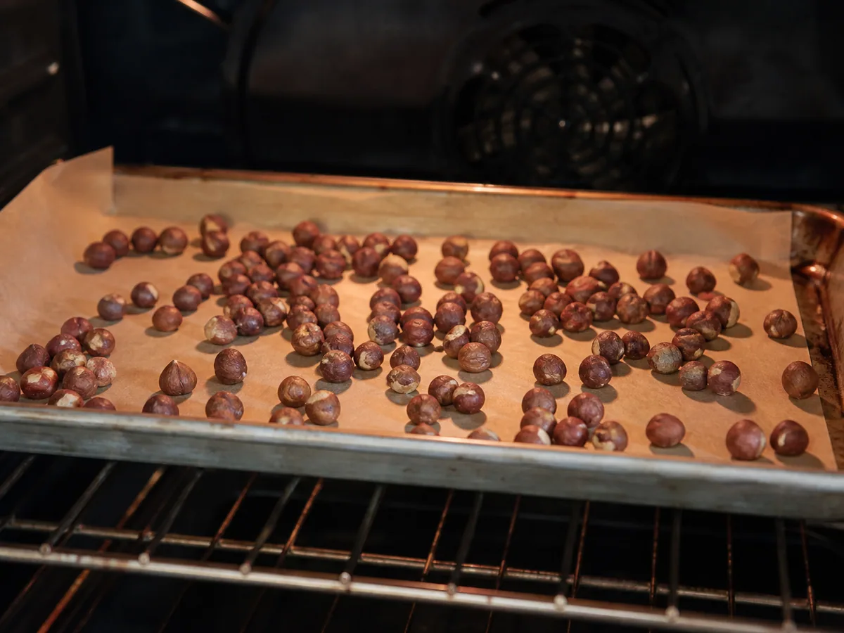 Roasted hazelnuts with dry, darkened skins on a parchment-lined baking sheet