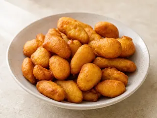 Plate of golden Jamaican festival fritters with crisp ridges and tapered ends