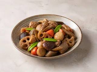 Chikuzenni japonés con pollo, raíz de loto, bardana, taro, zanahoria, shiitake, konnyaku y tirabeques en un tazón de cerámica