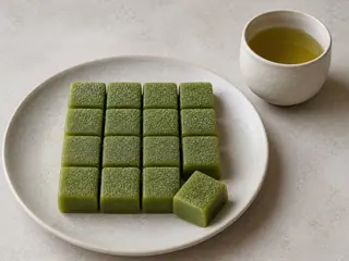 Pequeños cuadrados verdes de mochi de matcha, ligeramente espolvoreados con fécula de papa, sobre un plato de cerámica