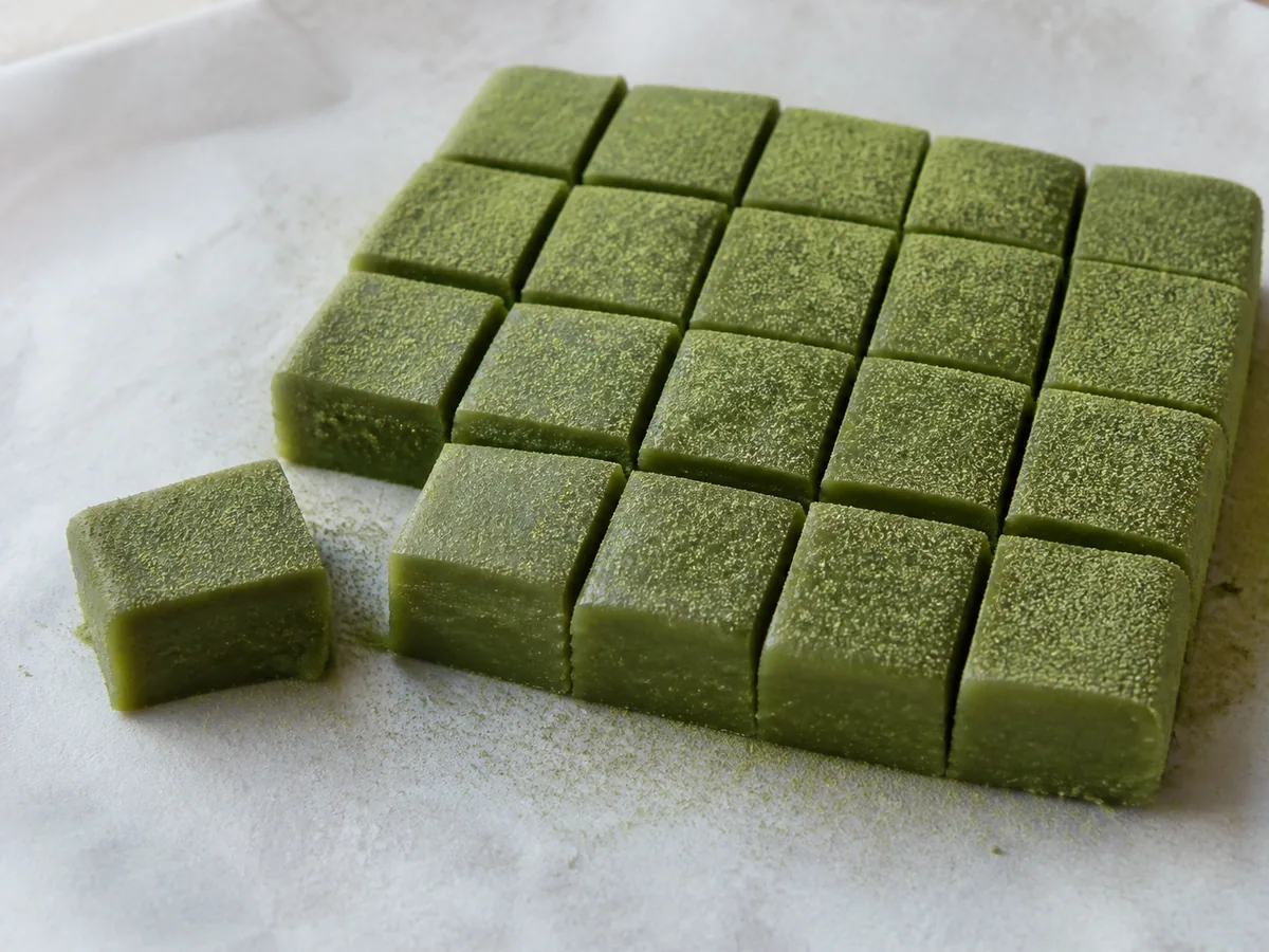 Dezesseis pedaços de mochi de matcha com as bordas recém-cortadas levemente cobertas de fécula de batata