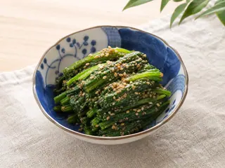 Espinaca japonesa con sésamo en un tazón pequeño de cerámica, cubierta con sésamo triturado