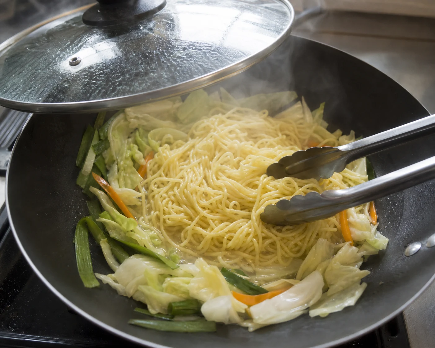 Fideos yakisoba cocidos al vapor, separados suavemente y mezclados con vegetales tiernos y crujientes antes de añadir la salsa