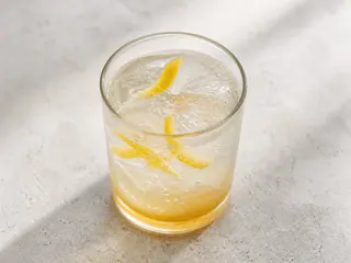 Vaso alto de refresco japonés de yuzu y miel con hielo y una espiral de cáscara de yuzu