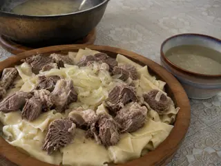 Kazakh beshbarmak with sliced beef, broad noodles, onions, and dill on a communal platter