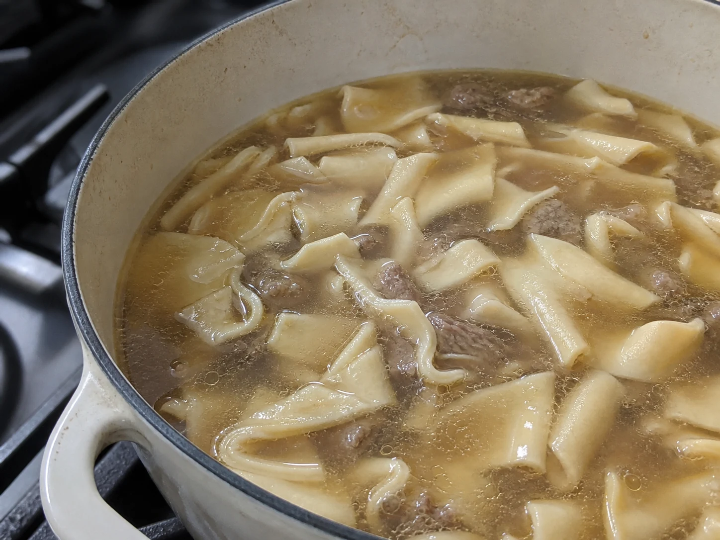 Retângulos largos de macarrão completamente cozidos sendo retirados do caldo para beshbarmak cazaque