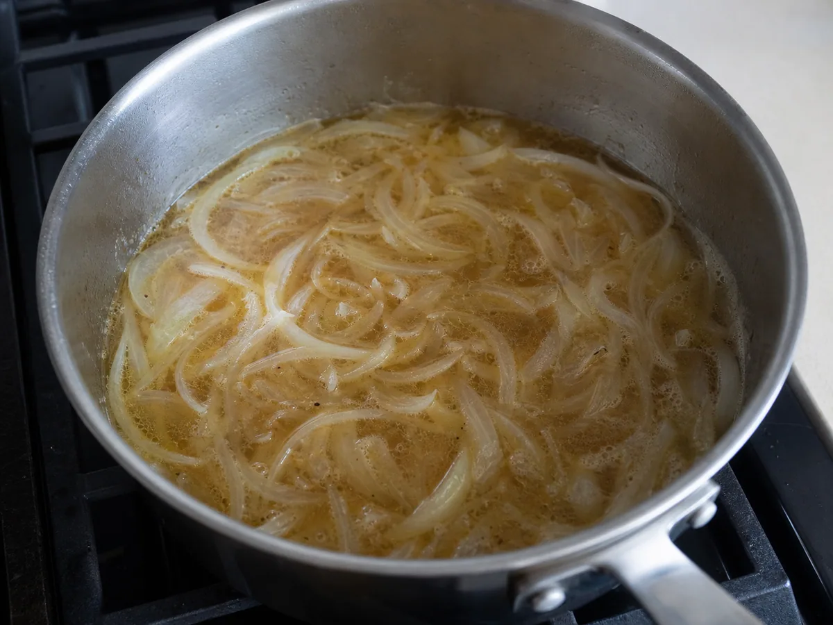 Meias-luas de cebola translúcidas amaciadas em caldo claro para beshbarmak cazaque
