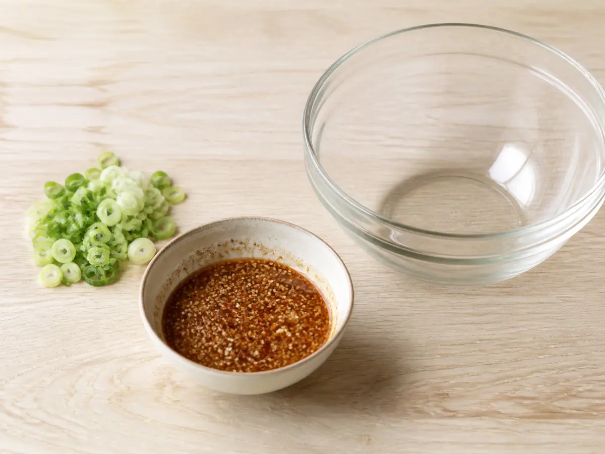 Red-speckled sesame dressing whisked in a small bowl beside sliced scallions