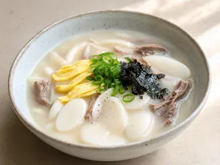Tazón de sopa coreana de pasteles de arroz con res, tiras de huevo, cebollín y gim tostado