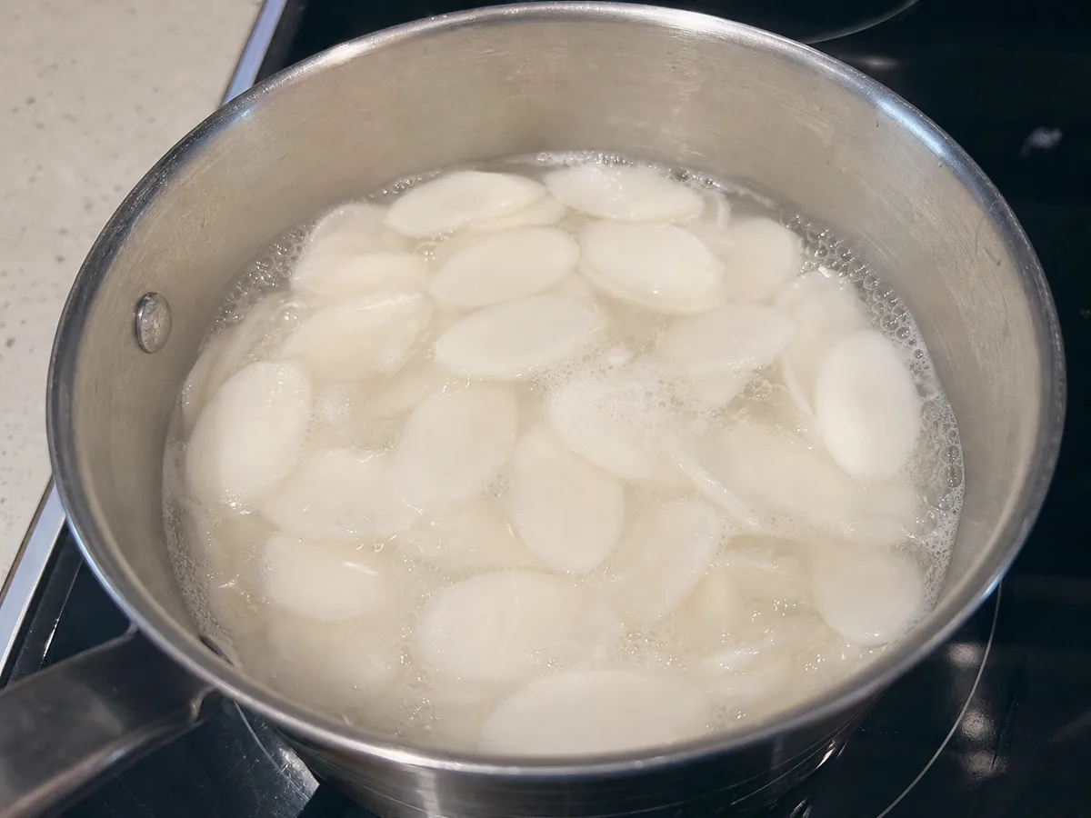 Pasteles de arroz ovalados floteo en caldo claro, suaves en los bordes pero todavía elásticos