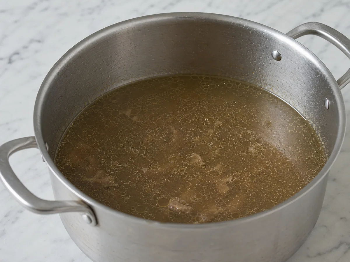Caldo de res claro en hervor suave después de retirar la espuma de la superficie
