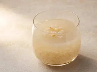 Vaso de vidrio transparente con sikhye coreano, granos de arroz flotantes, piñones y azufaifa