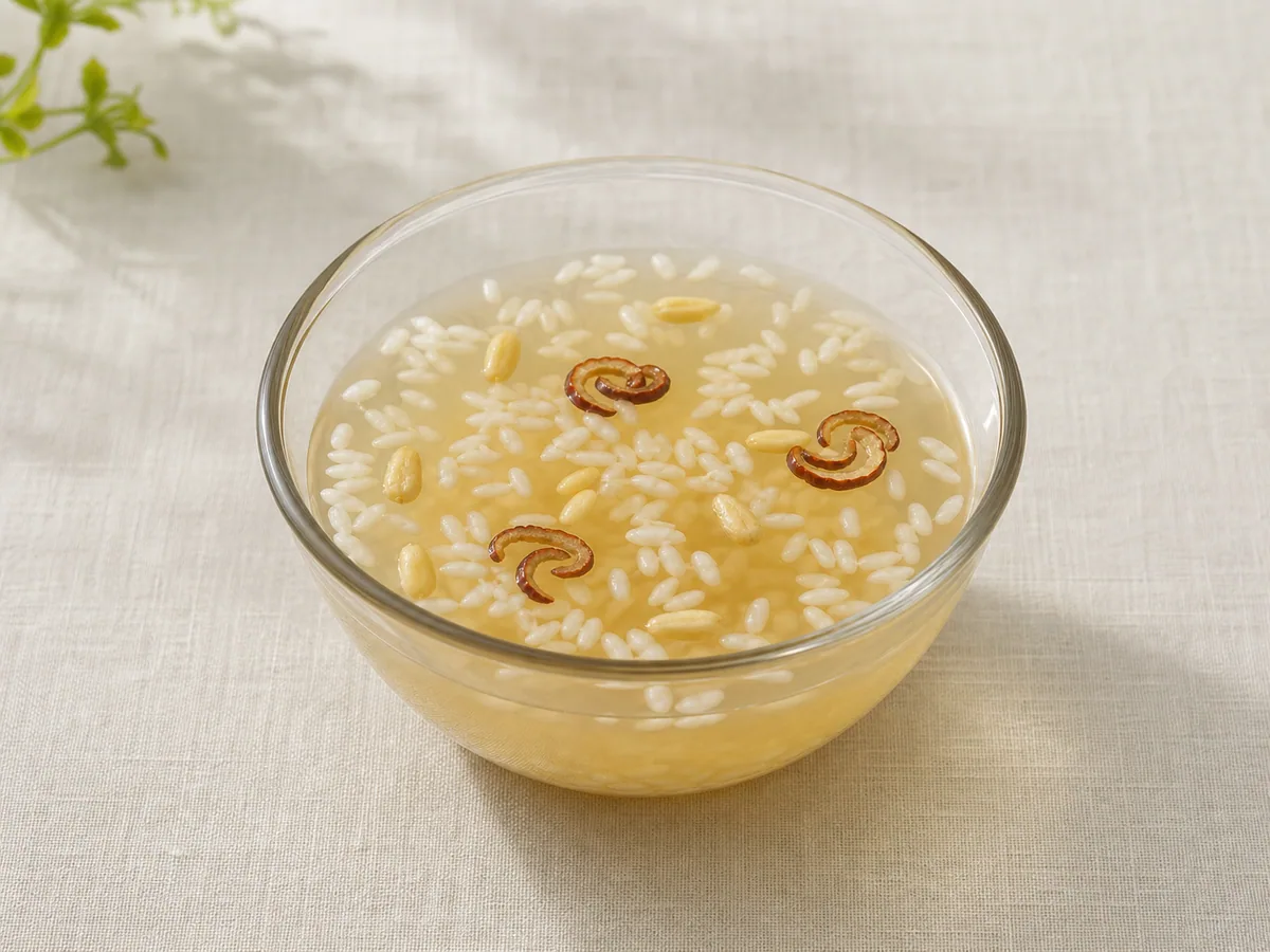 Copo transparente de sikhye coreano com grãos de arroz flutuantes, pinhões e azufaifa