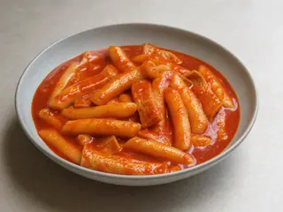 Tazón ancho de tteokbokki coreano con salsa roja brillante, pastel de pescado, repollo, cebollín y semillas de sésamo
