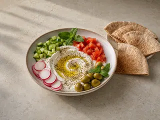 Tazón libanés de labneh para el desayuno, con vegetales, aceitunas, za'atar y pan pita