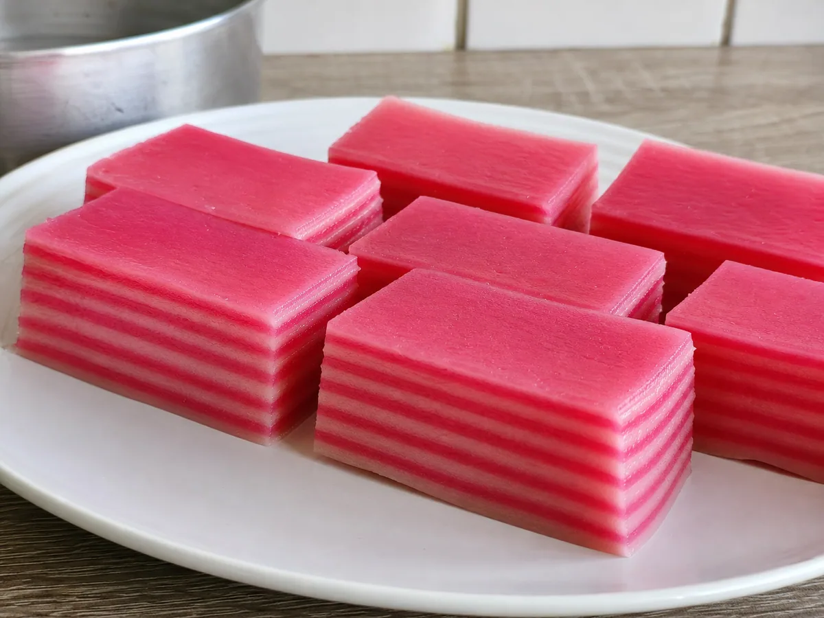 Fatias rosas e brancas de kuih lapis malaio mostrando nove camadas cozidas no vapor