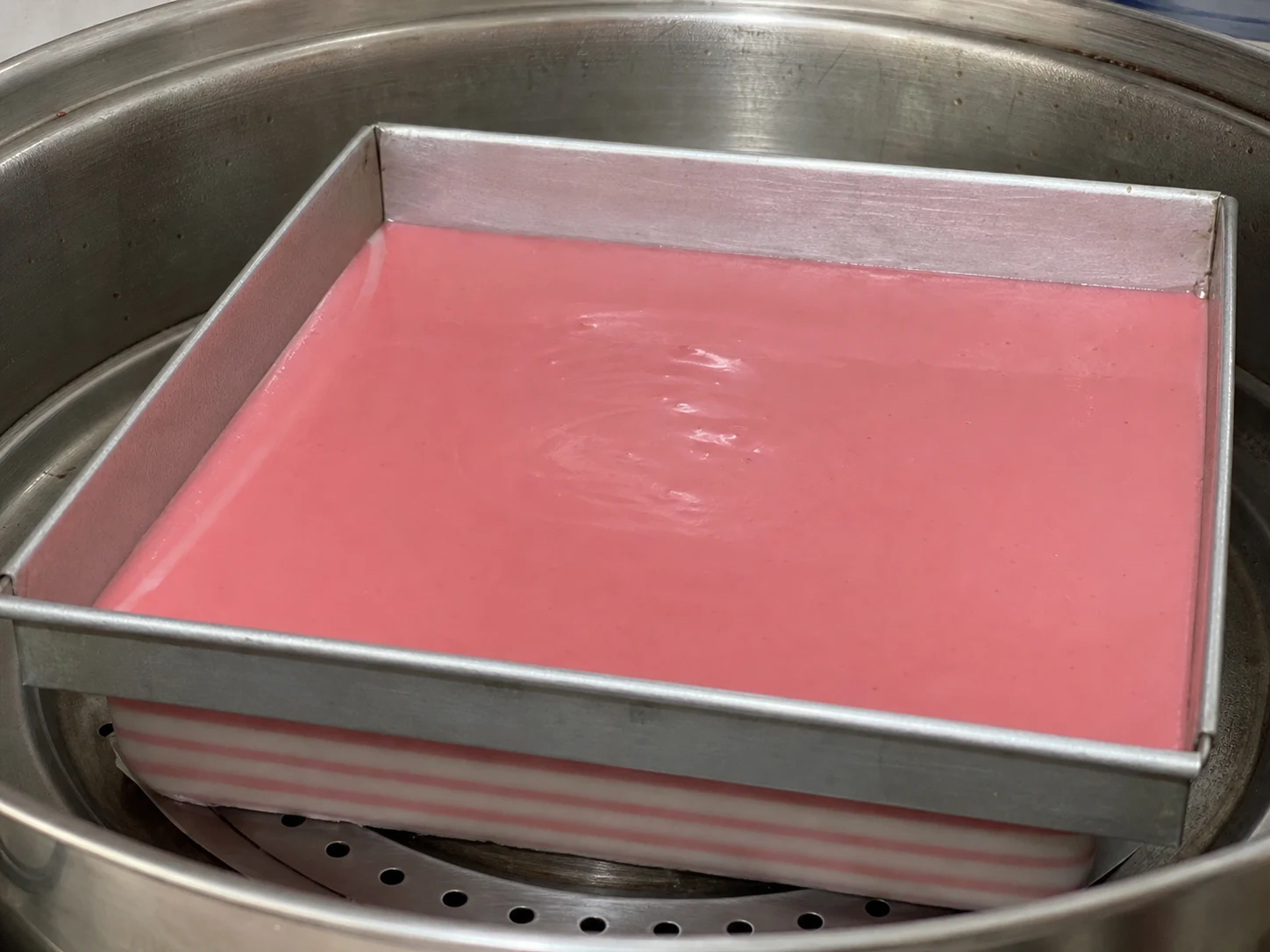 Eight set alternating pink and white layers of Malaysian kuih lapis in the steaming pan