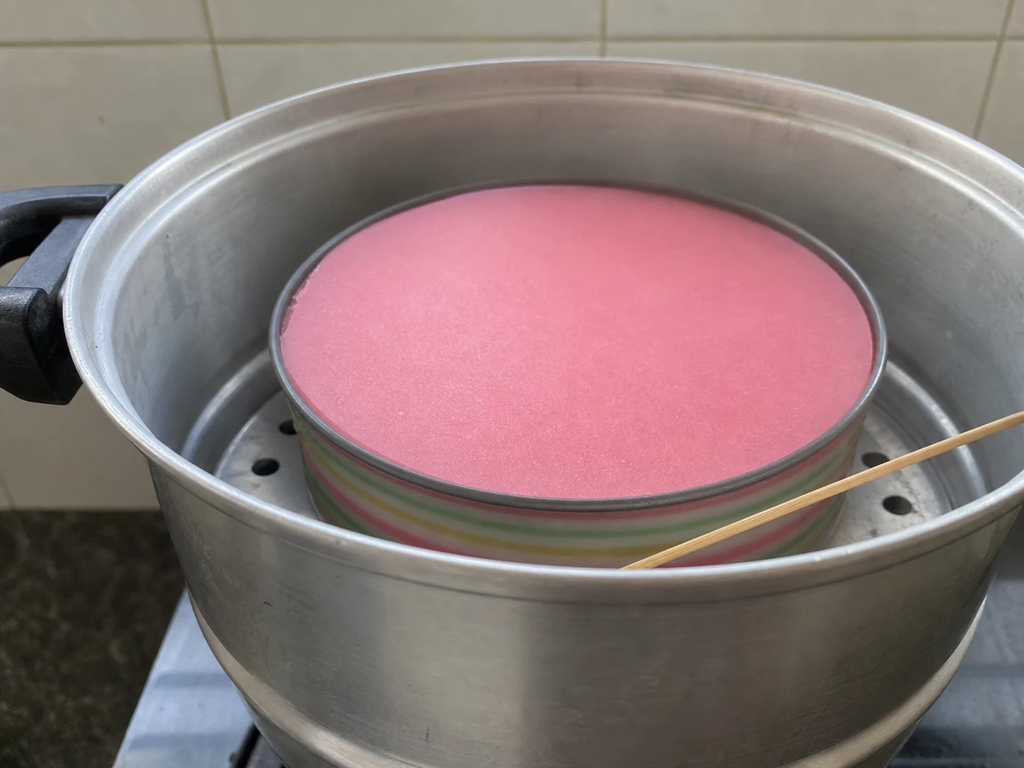 Fully set ninth pink layer of Malaysian kuih lapis releasing slightly from the pan edge