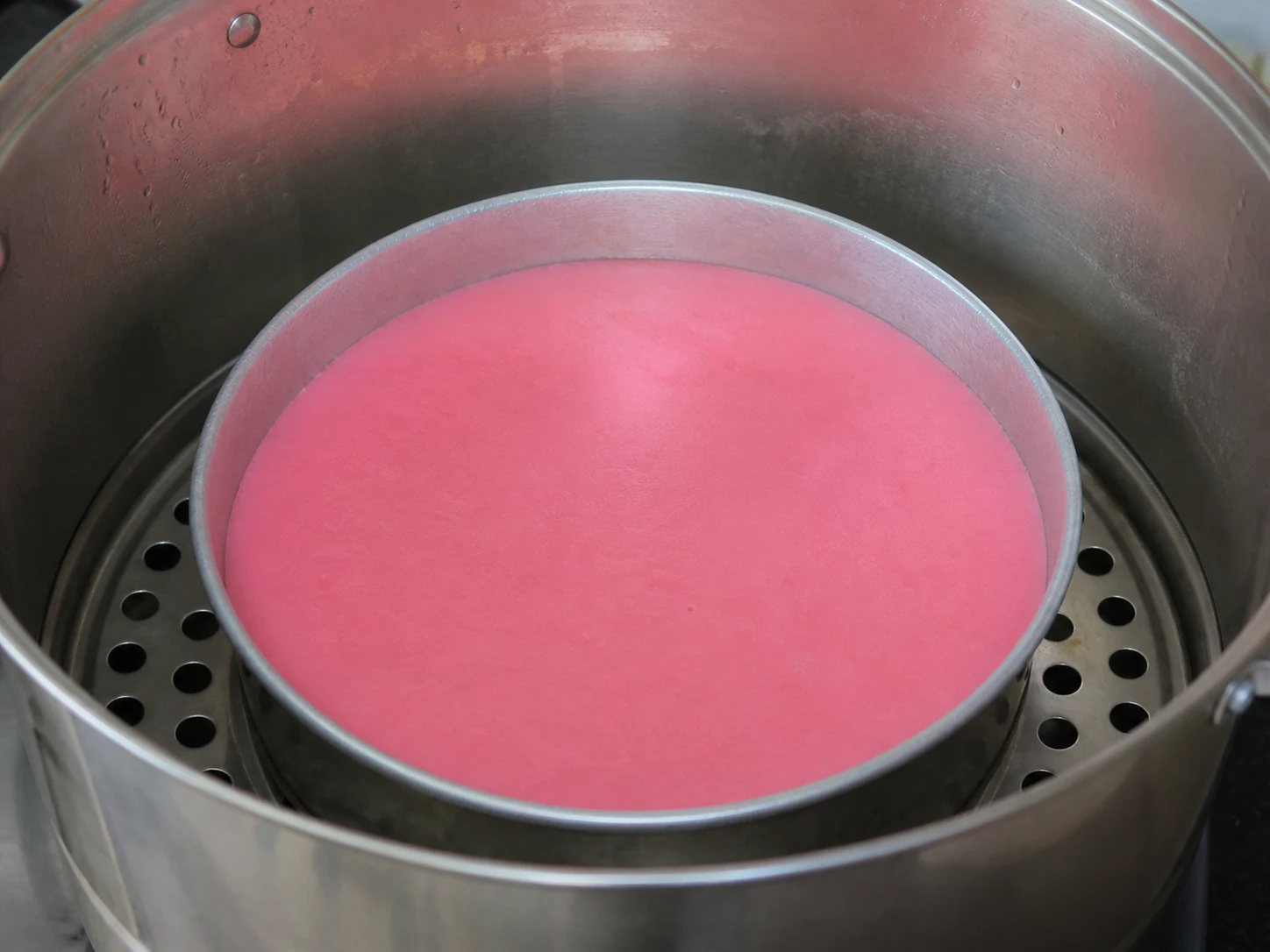 First thin pink layer of Malaysian kuih lapis set in a round steaming pan