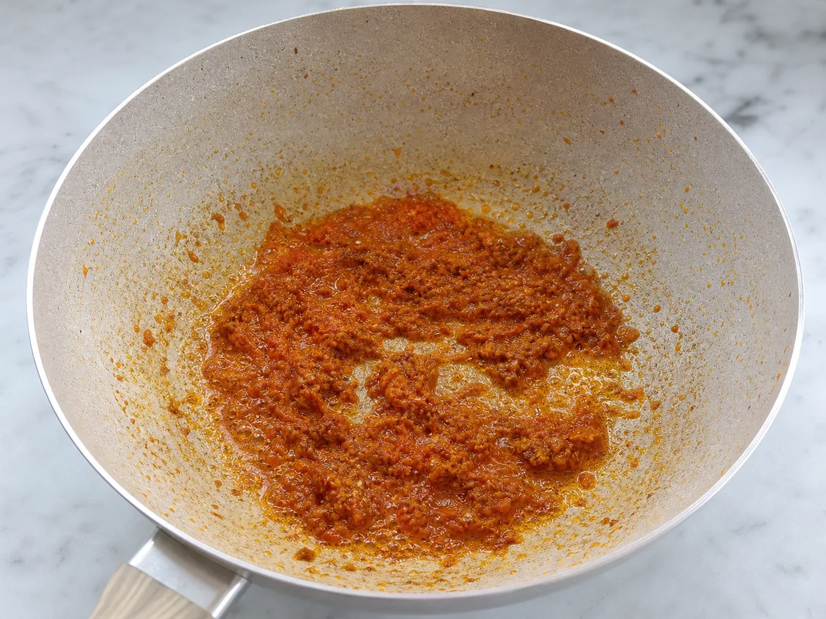 Pasta de especiarias da laksa malaia escurecida, com pequenas gotas de óleo em uma panela pesada