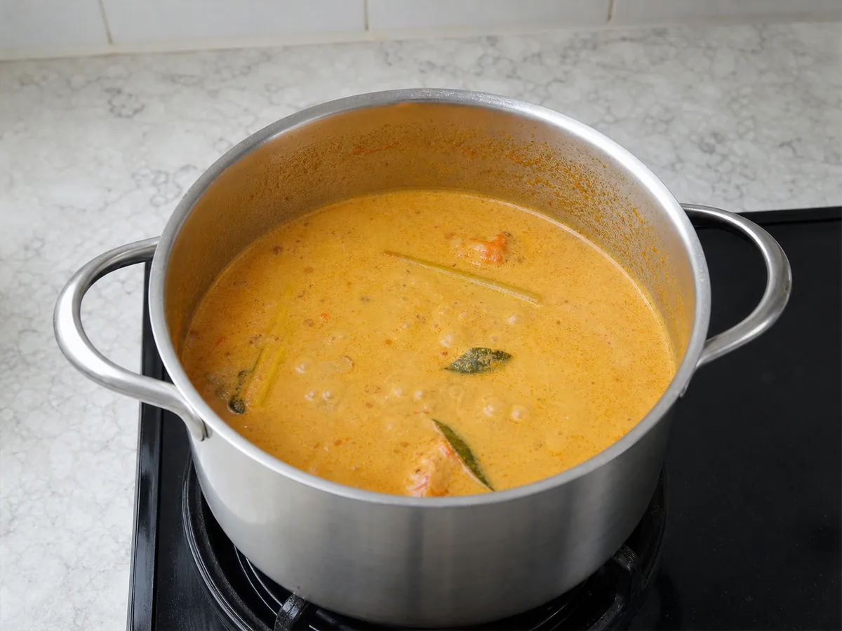 Caldo laranja-dourado e homogêneo de laksa malaia borbulheo suavemente ao redor do tofu frito