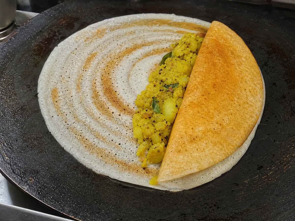 Dosa crujiente doblada sobre relleno de papa especiado en una plancha caliente