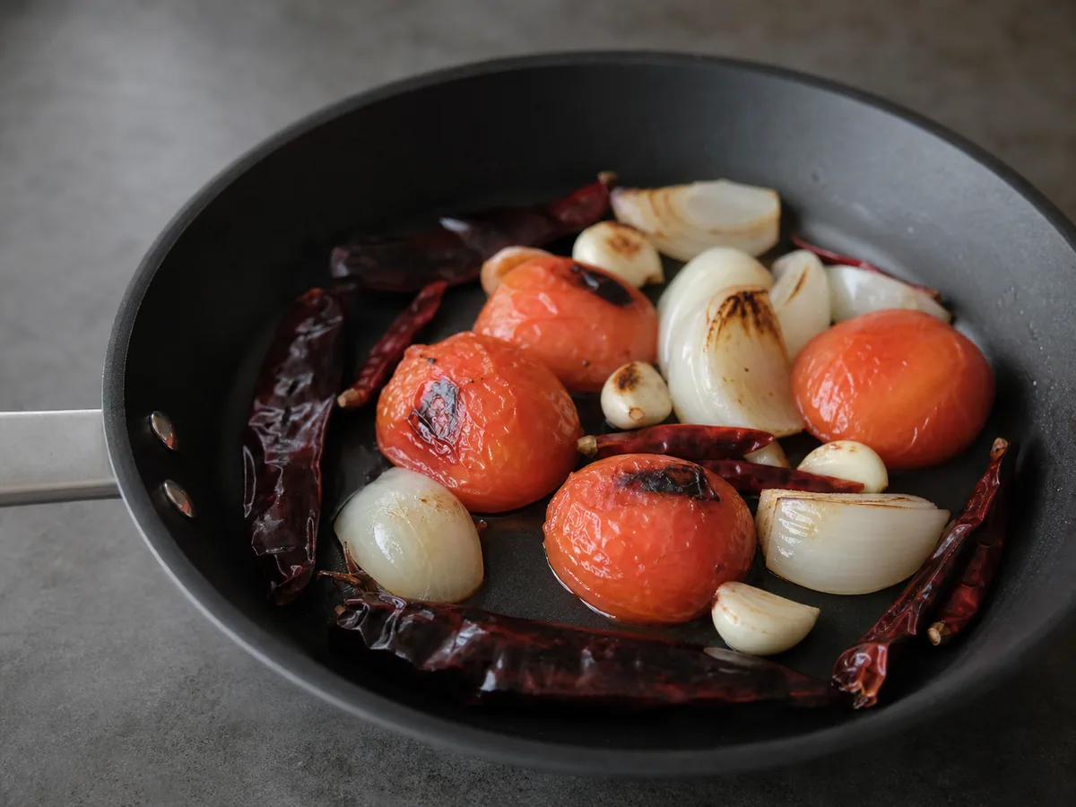 Tomates amolecidos, cebola, alho e pimentas guajillo flexíveis cozinhando em uma panela