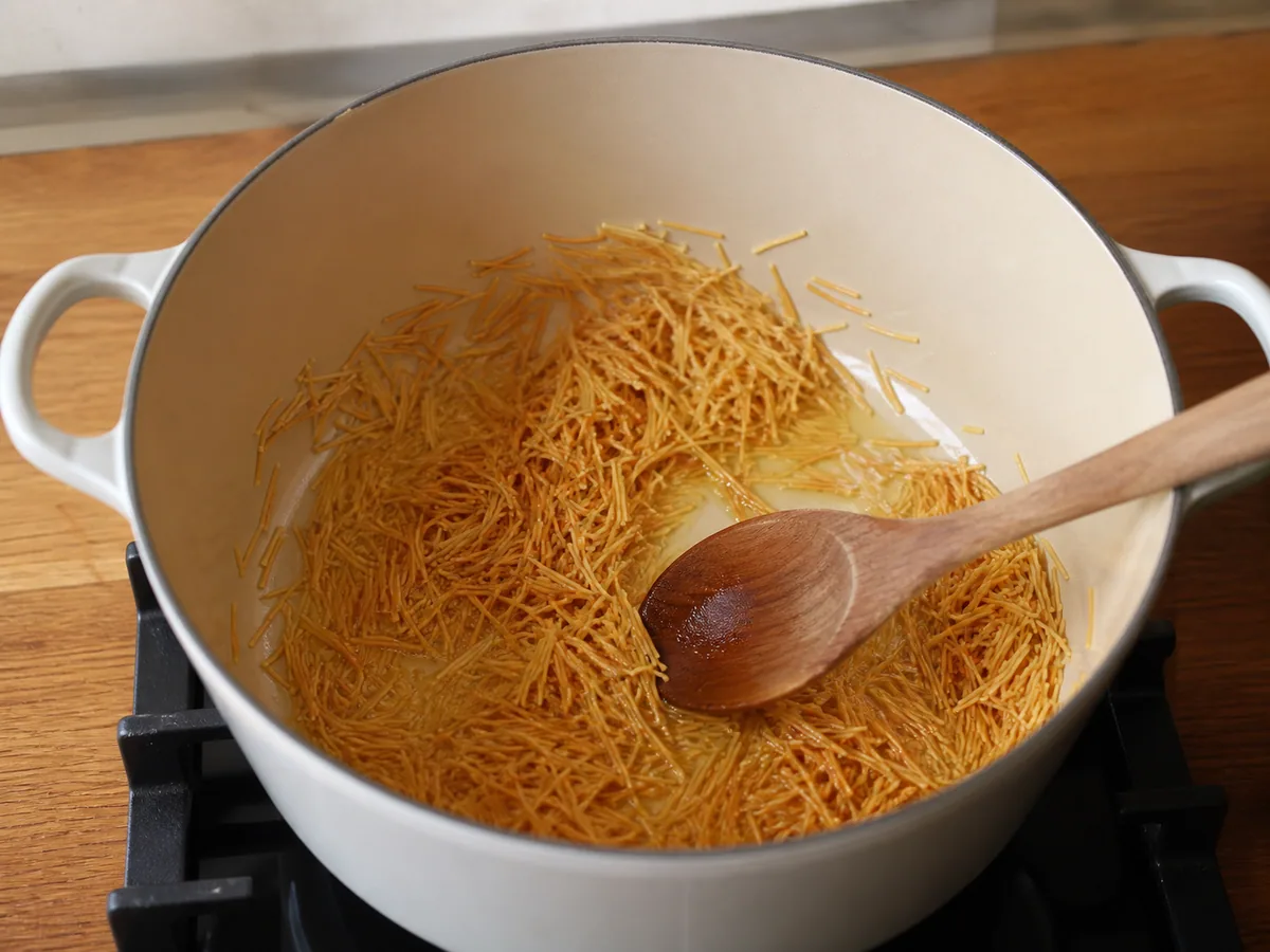 Macarrão fideo dourado-claro tostando em óleo vegetal em uma panela de sopa pesada