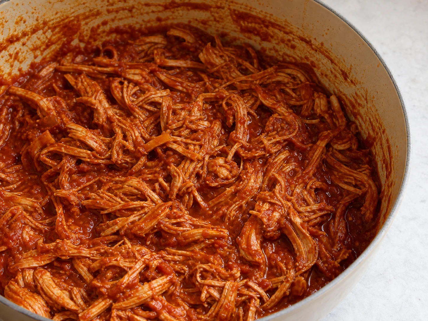 Frango desfiado completamente cozido, coberto por molho espesso de tinga de tomate e chipotle