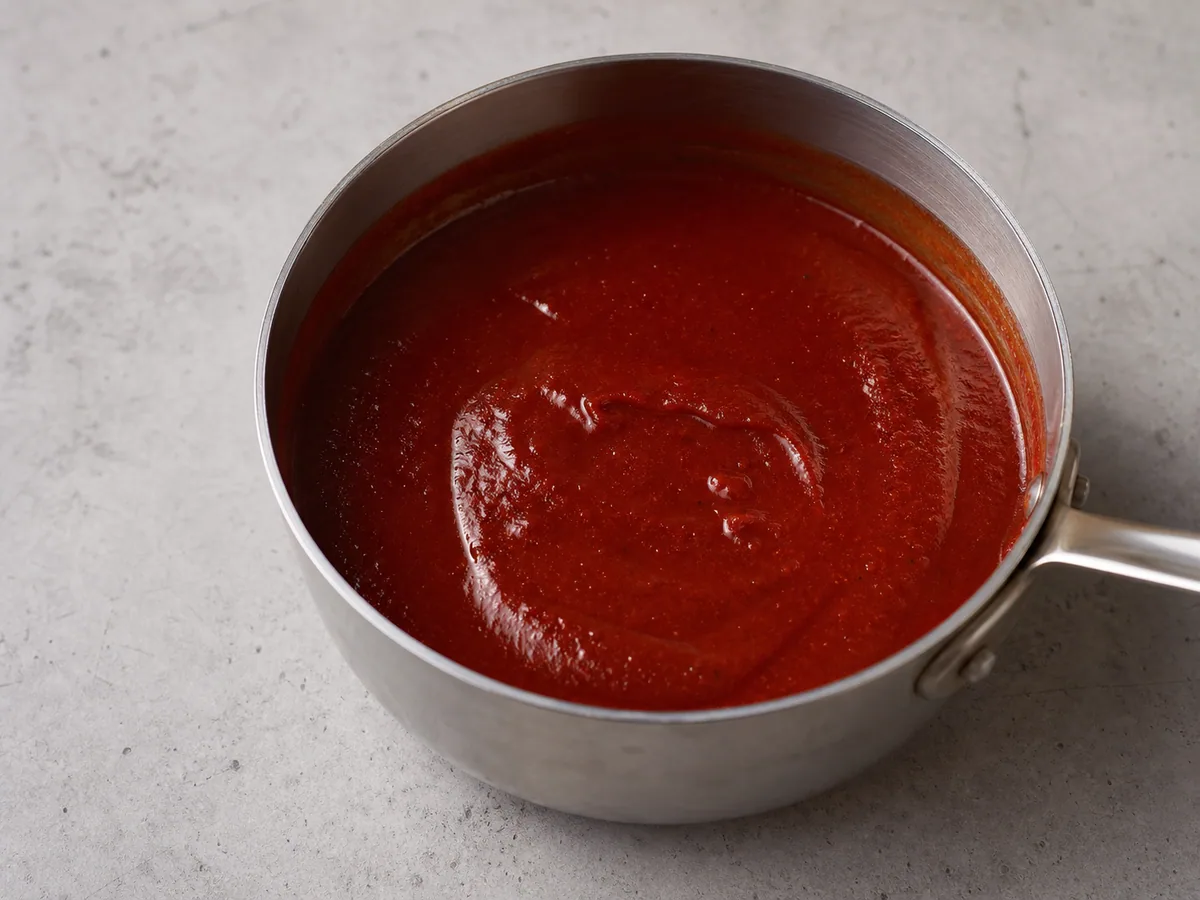 Salsa suave de guajillo y ancho para enchiladas cubriendo ligeramente una cuchara en una cacerola