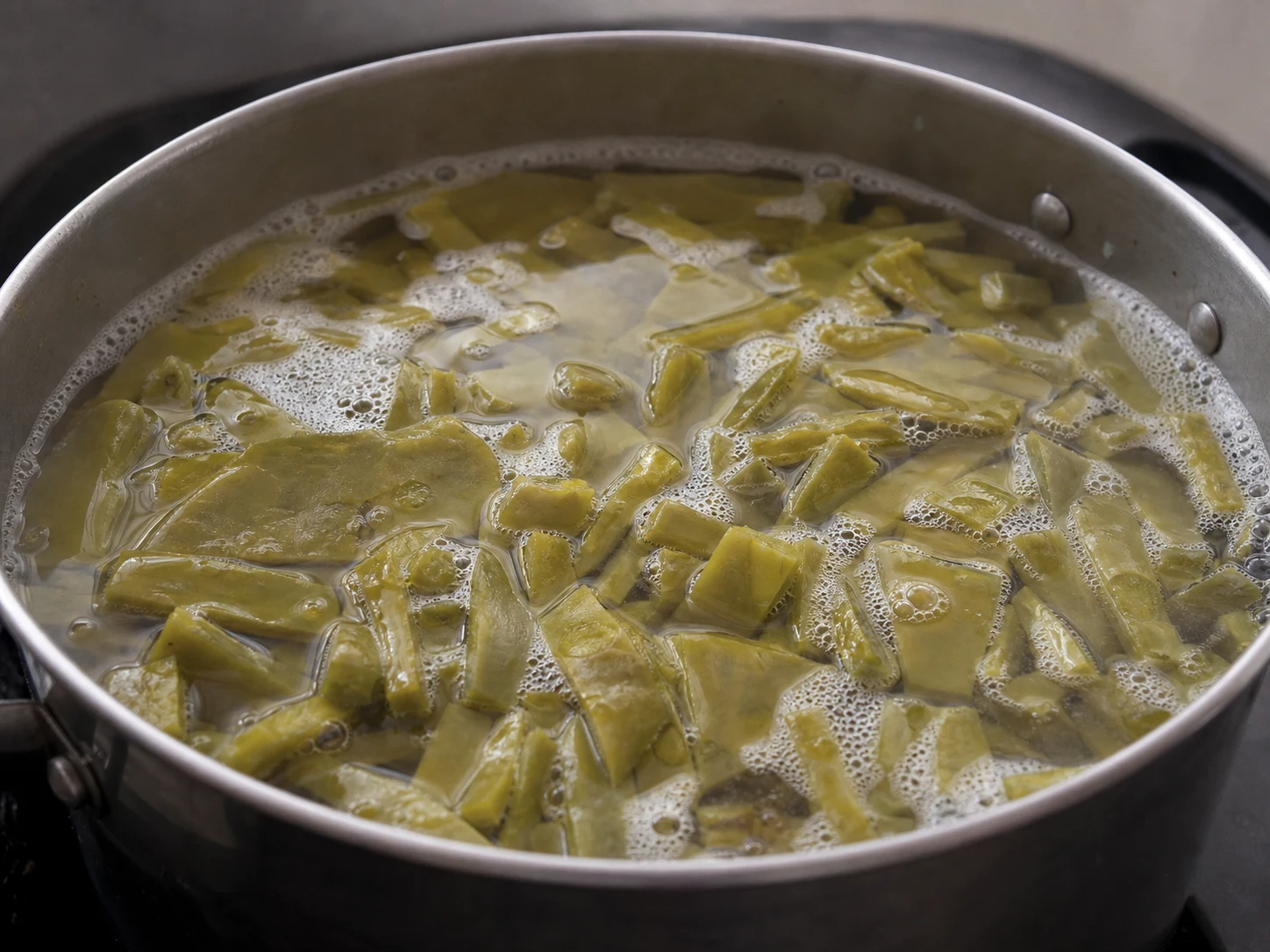Nopales cortados cozinhando em líquido levemente espumoso até ficarem verde-oliva suave e macios