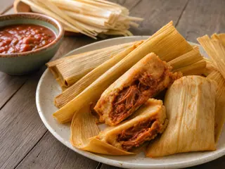 Tamales mexicanos de cerdo con chile rojo parcialmente abiertos para mostrar la masa y el relleno de cerdo deshebrado