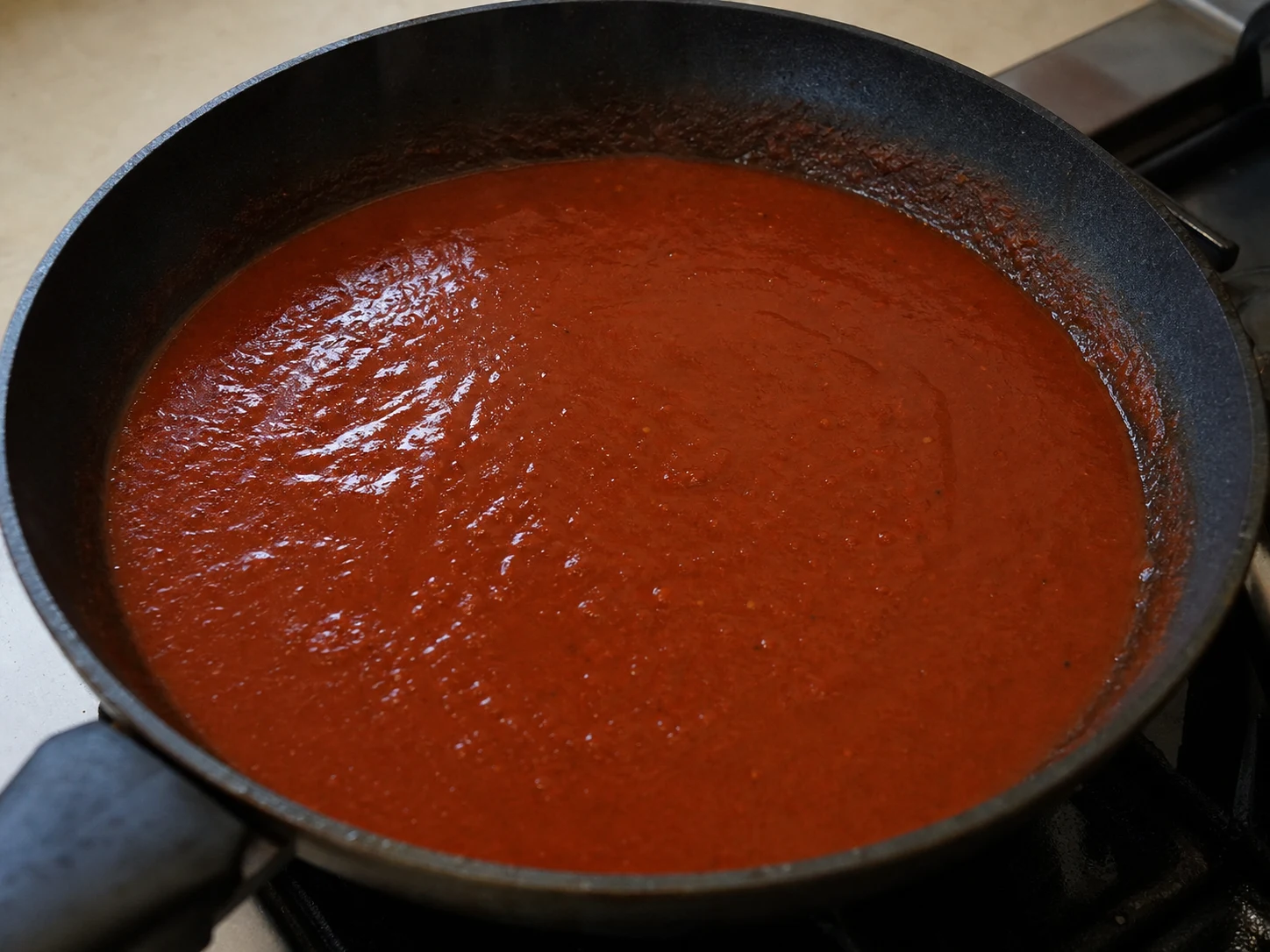 Smooth brick-red guajillo-ancho chile sauce leaving a brief spoon trail in a skillet for pork tamales
