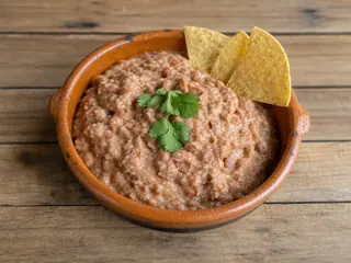 Frijoles refritos mexicanos de pinto, cremosos, en un tazón bajo de barro