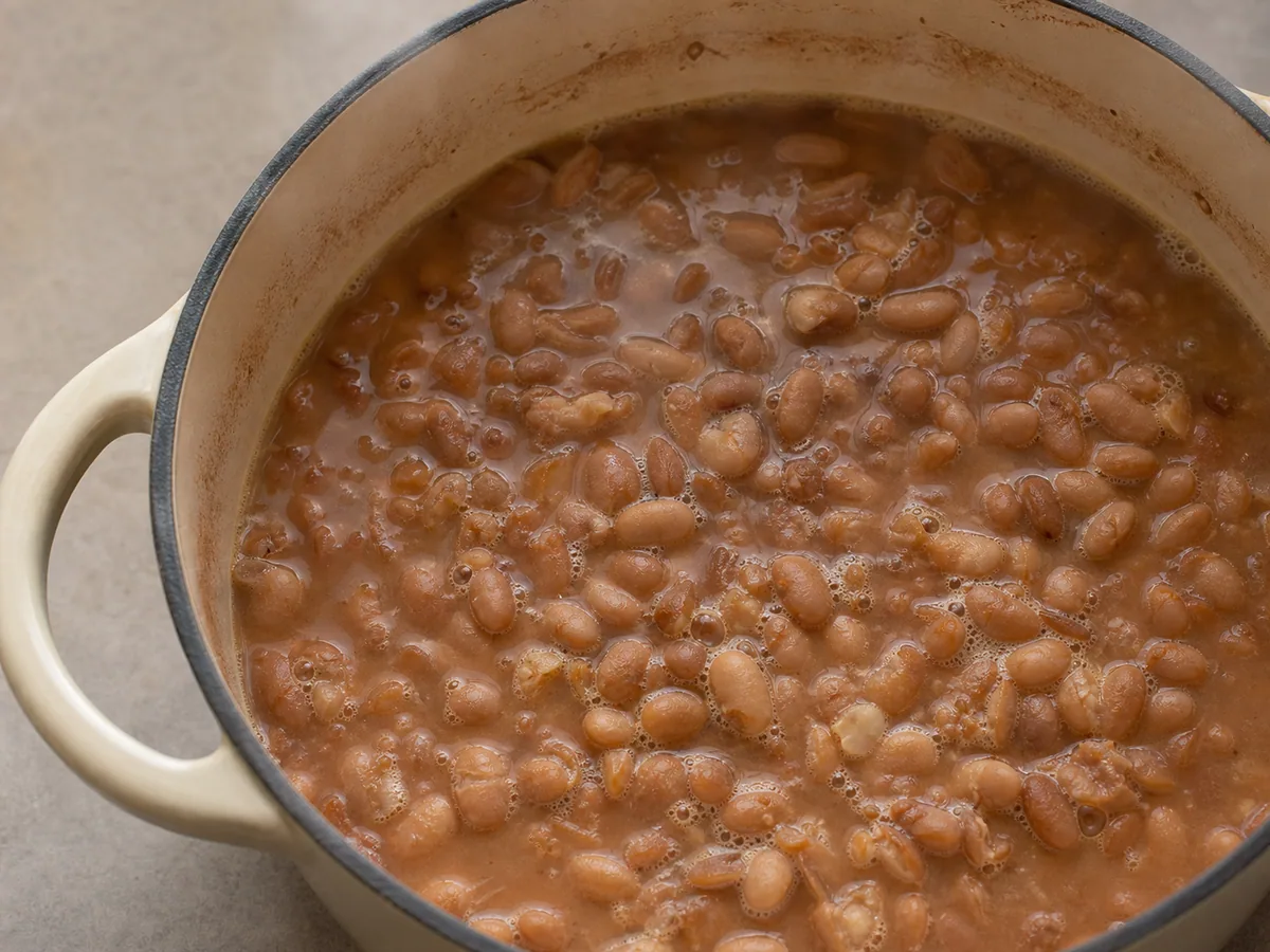 Frijoles pintos completamente tiernos cocinándose a fuego lento en una olla pesada, con los centros cremosos visibles