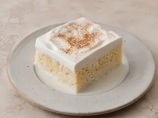 Porción cuadrada de pastel mexicano de tres leches con crema batida y canela