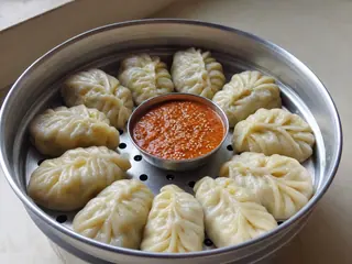 Momos nepaleses de verduras al vapor dispuestos alrededor de achar de tomate y ajonjolí