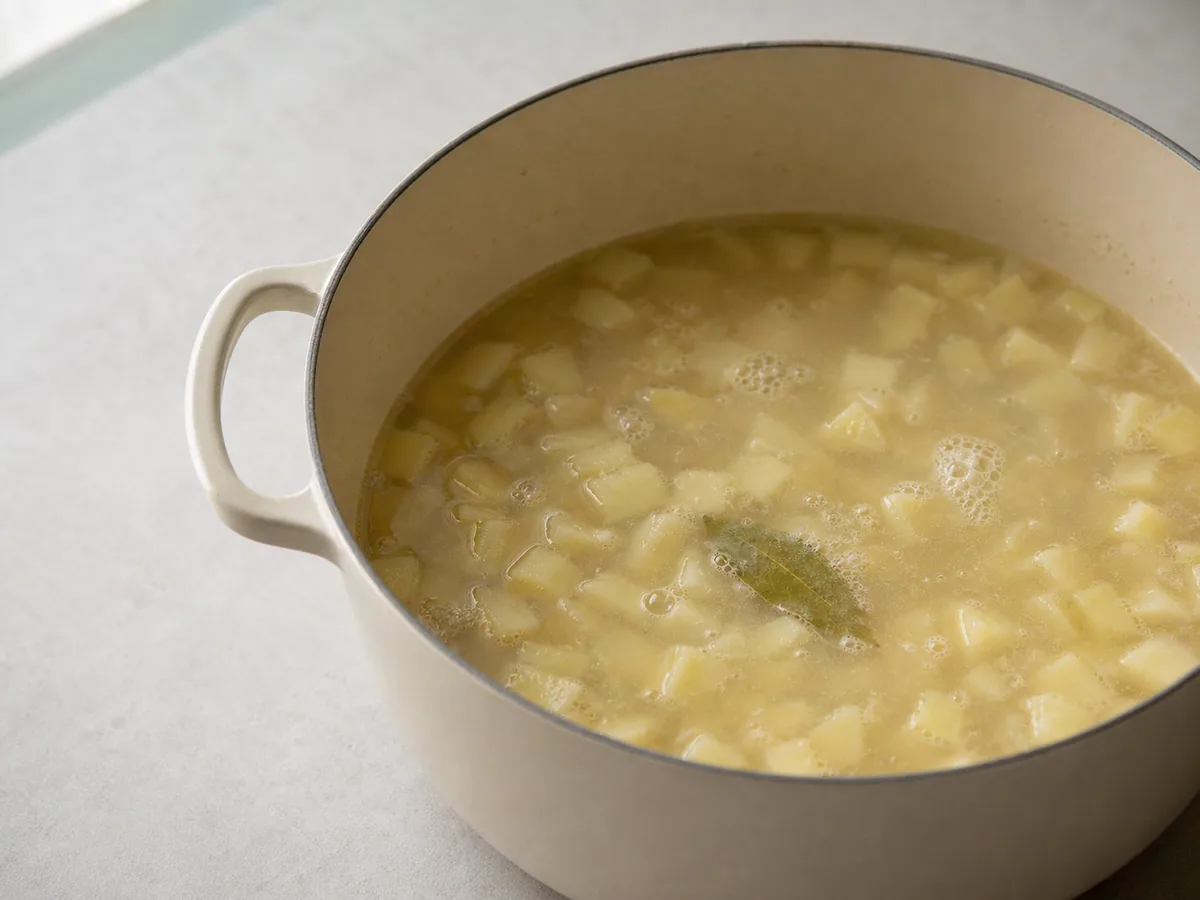 Cubos tiernos de papa Yukon Gold de media pulgada cocinándose en la base pálida de la sopa