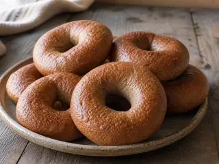 Caraway-topped rye bagels with a glossy brown crust and one bagel split to show the chewy crumb
