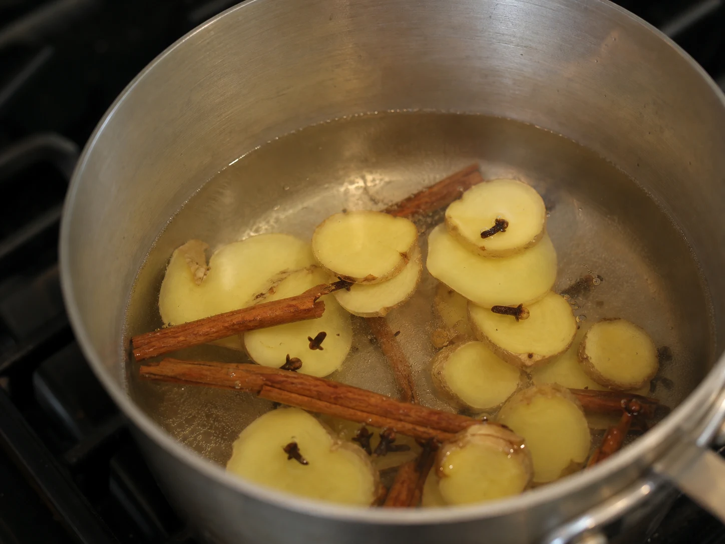 Paus de canela, cravos-da-índia inteiros e gengibre fresco fatiado fervendo suavemente em água para o ponche de maçã, canela e rooibos