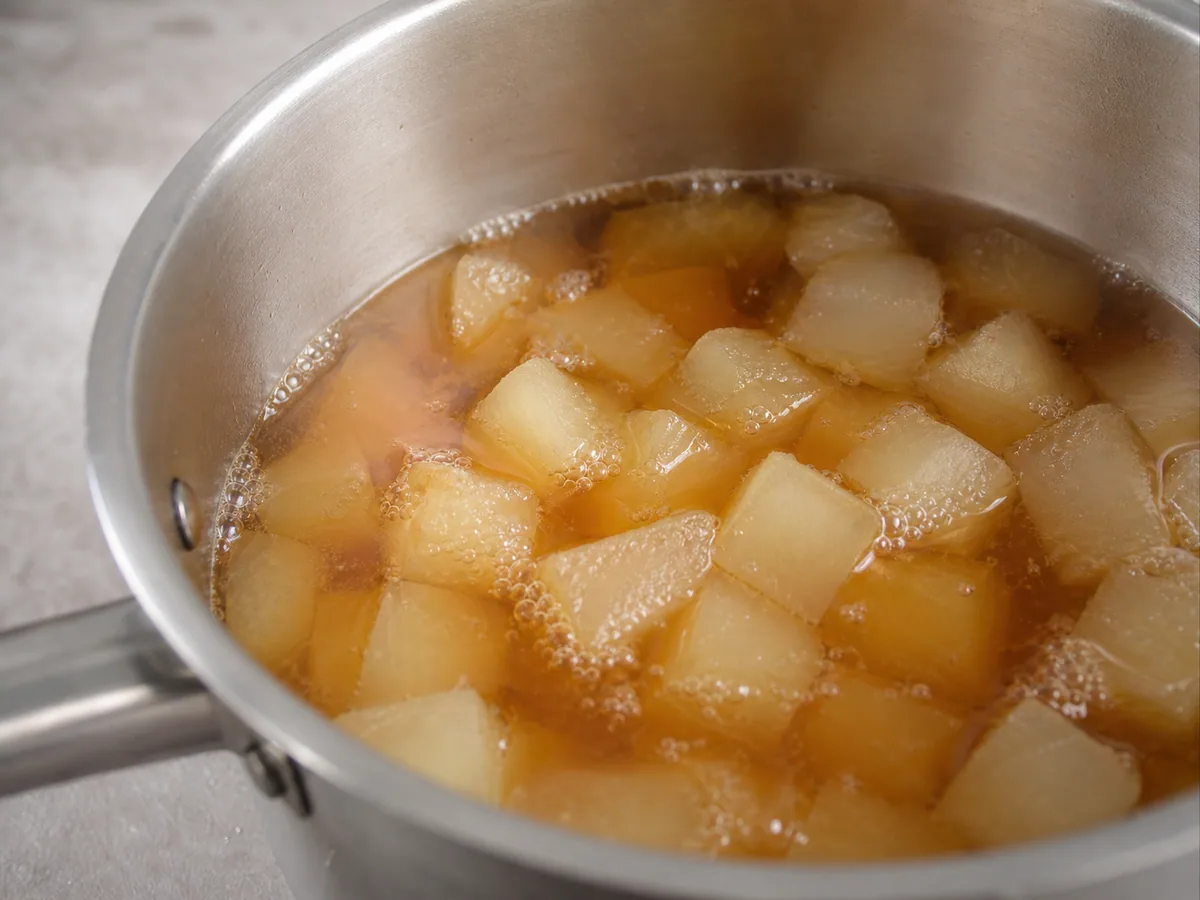 Cubos translúcidos de melón de invierno cociéndose suavemente en té claro de azúcar morena ámbar