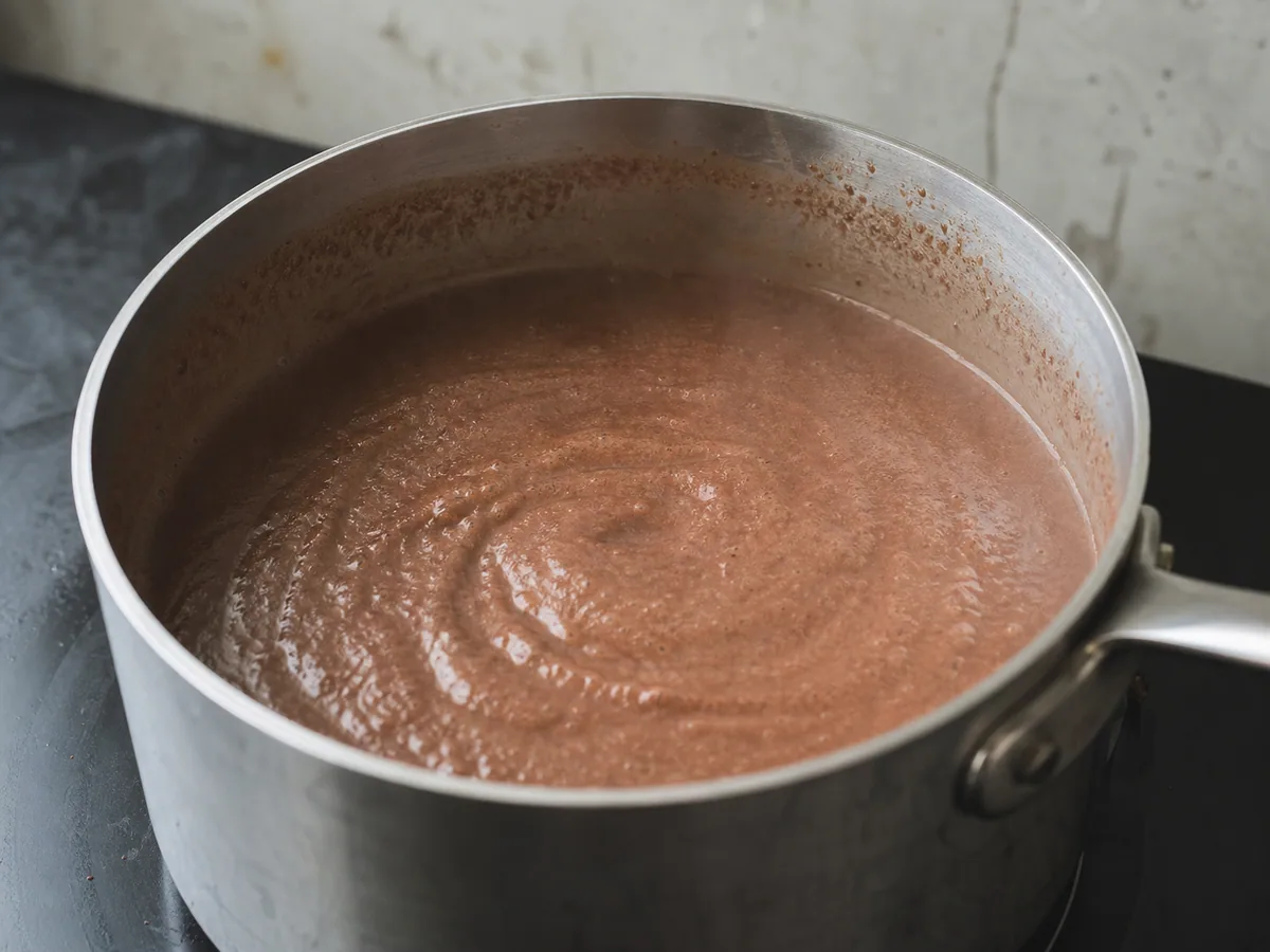 Thickened Mexican cinnamon champurrado dripping from a coated whisk over a saucepan