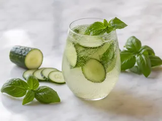 Vaso alto de tónico espumoso de pepino y albahaca con hielo y una cinta de pepino