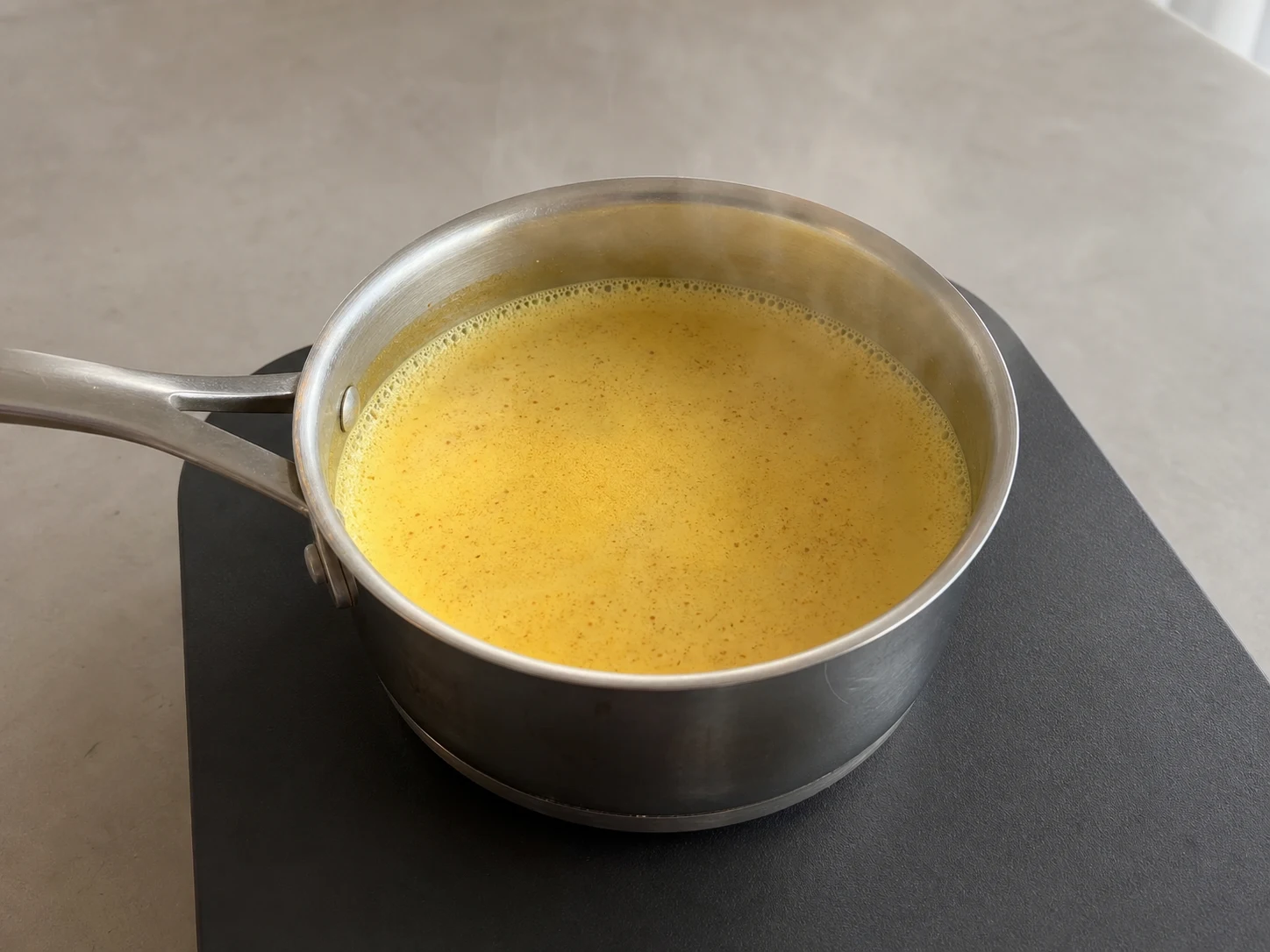Leche dorada de cúrcuma humeante con espuma ligera en los bordes de la cacerola antes de hervir