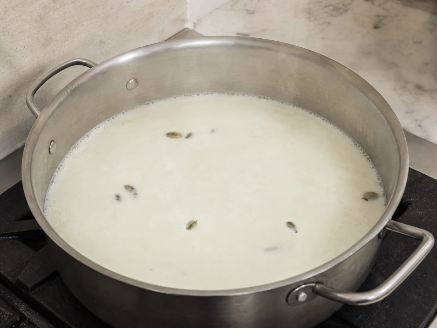 Whole milk with split cardamom pods reaching a gentle simmer for Pakistani cardamom rice kheer