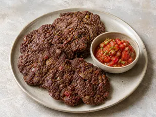Chapli kebabs pakistaníes con bordes dorados y crujientes junto a chutney de tomate troceado